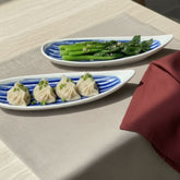 Two oval plates with dumplings and green vegetables on a textured surface.